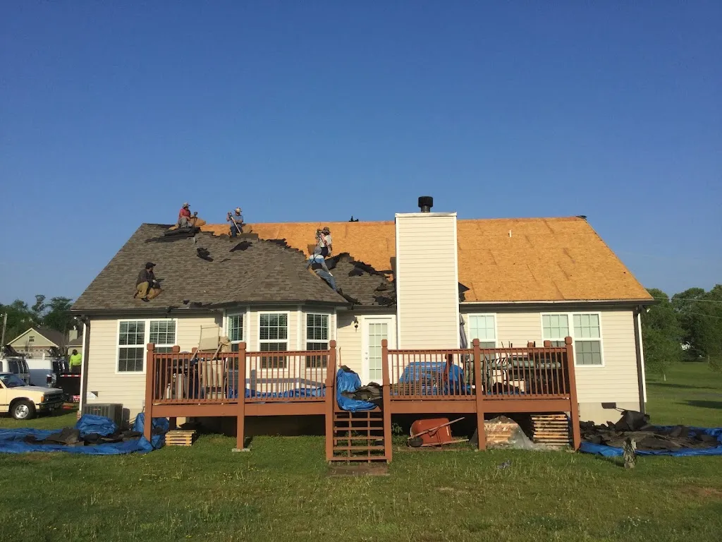 Hill Top Roofing crew tearing off a storm-damaged roof with tarps protecting the landscaping